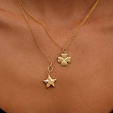 Gold necklace with a clover and star pendant on a person's neck.