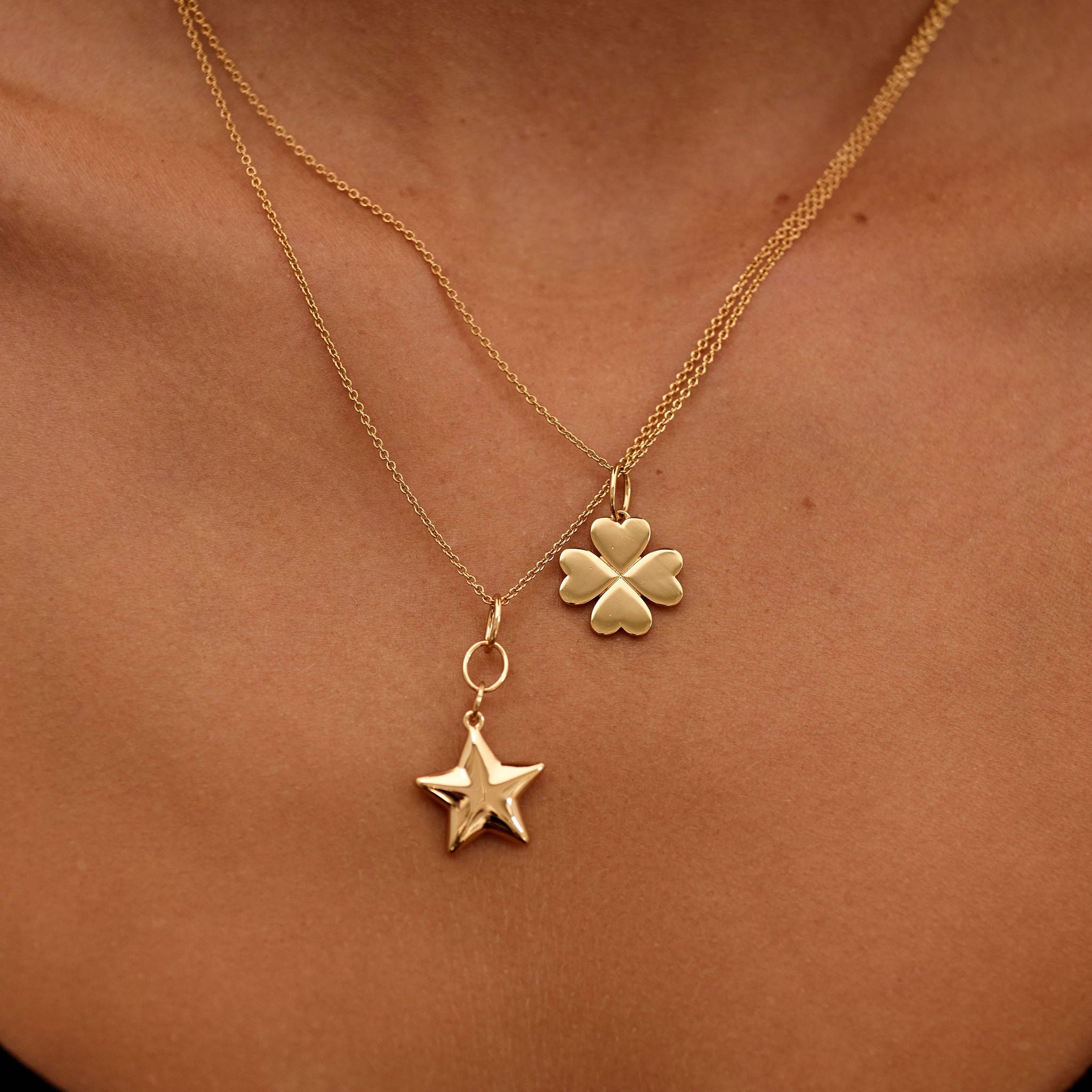 Gold necklace with a clover and star pendant on a person's neck.