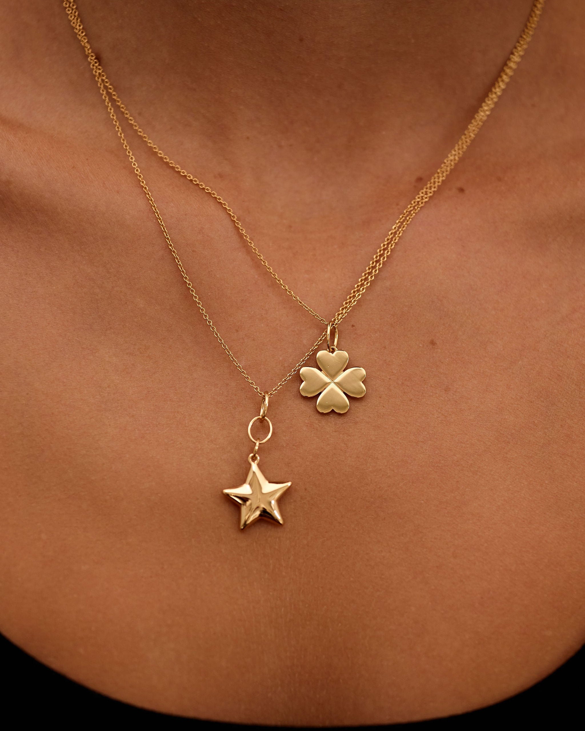 Gold necklace with a clover and star pendant on a person's neck.