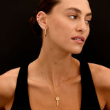 Woman wearing a gold key-shaped necklace against a black background