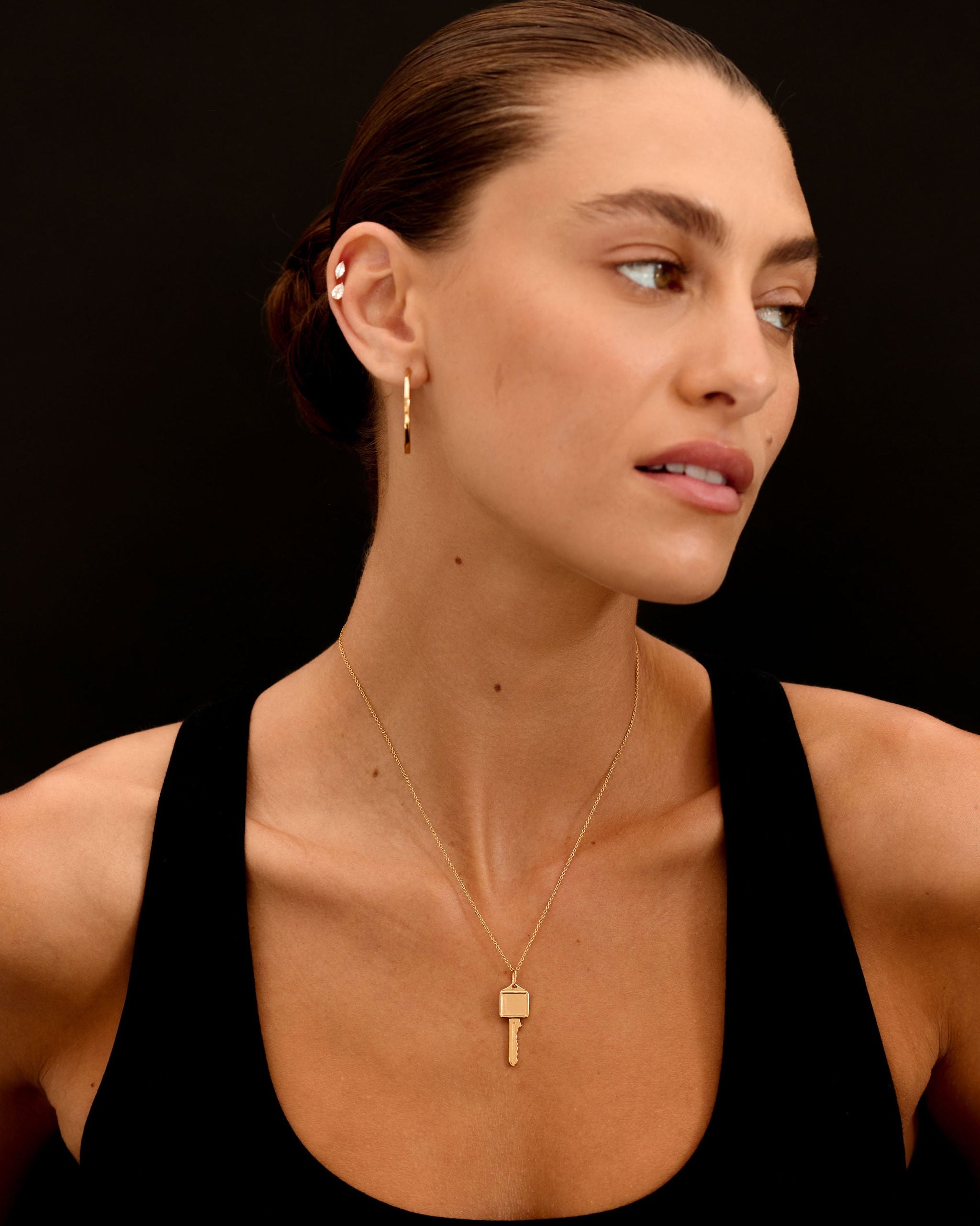 Woman wearing a gold key-shaped necklace against a black background