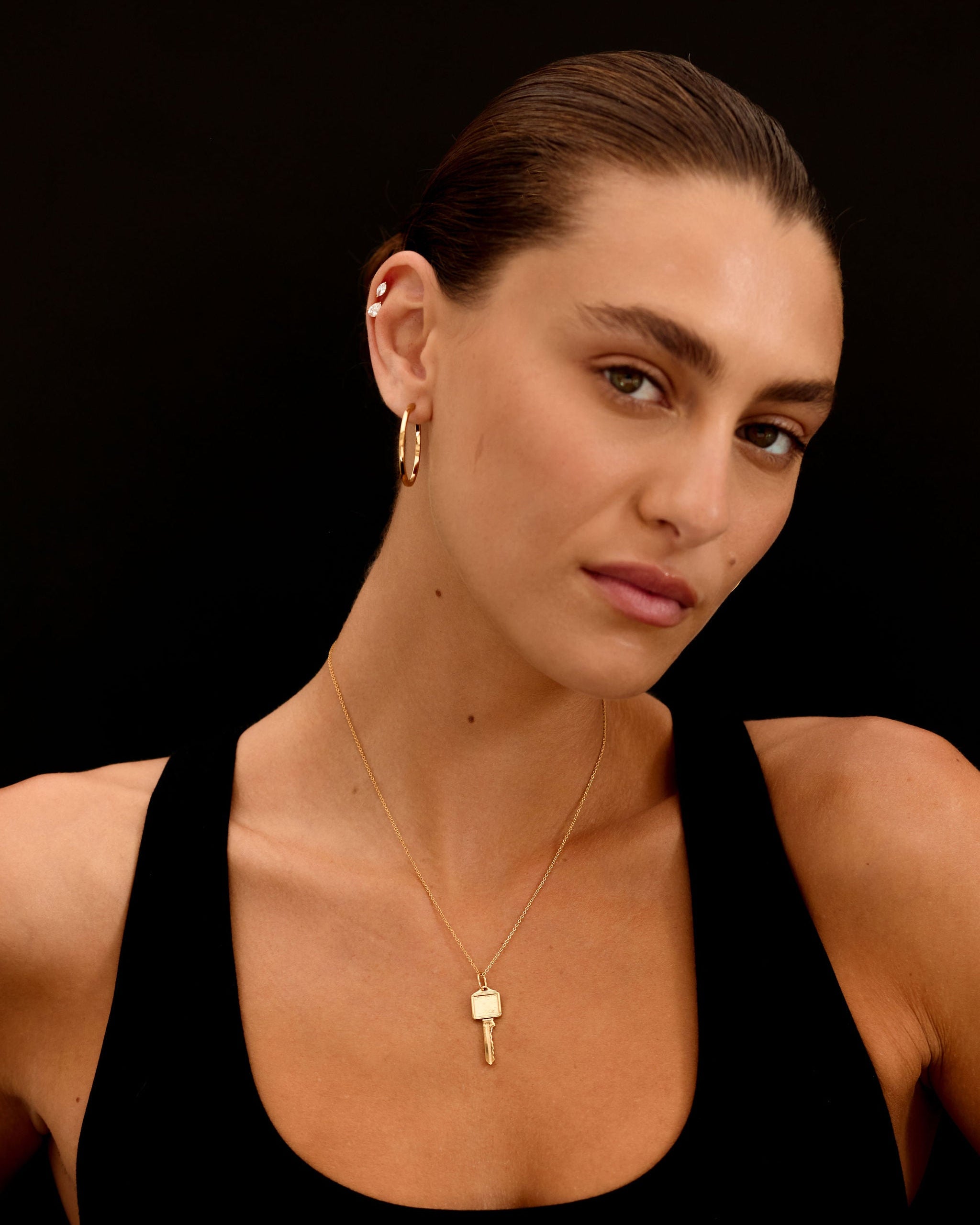 Woman wearing a black top and gold jewelry against a black background