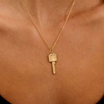 Gold necklace with a key pendant on a person's neck against a black background