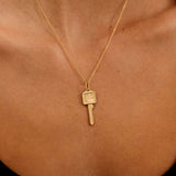 Gold necklace with a key pendant on a person's neck against a black background