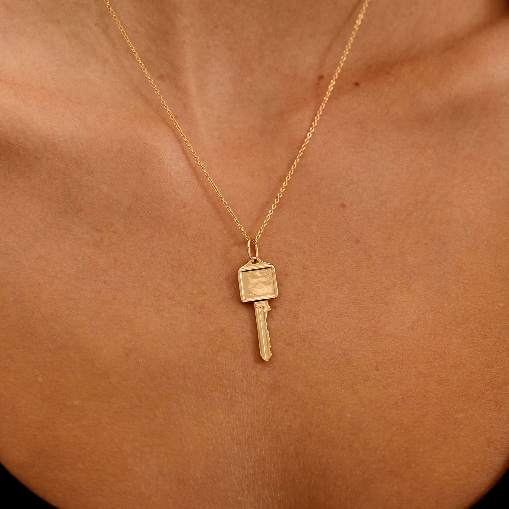 Gold necklace with a key pendant on a person's neck against a black background