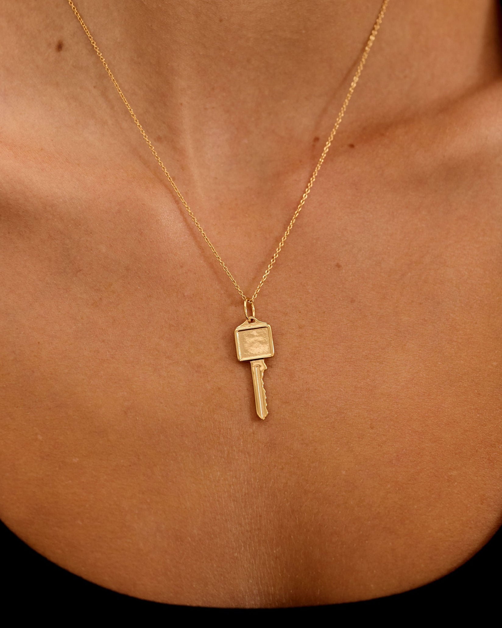 Gold necklace with a key pendant on a person's neck against a black background
