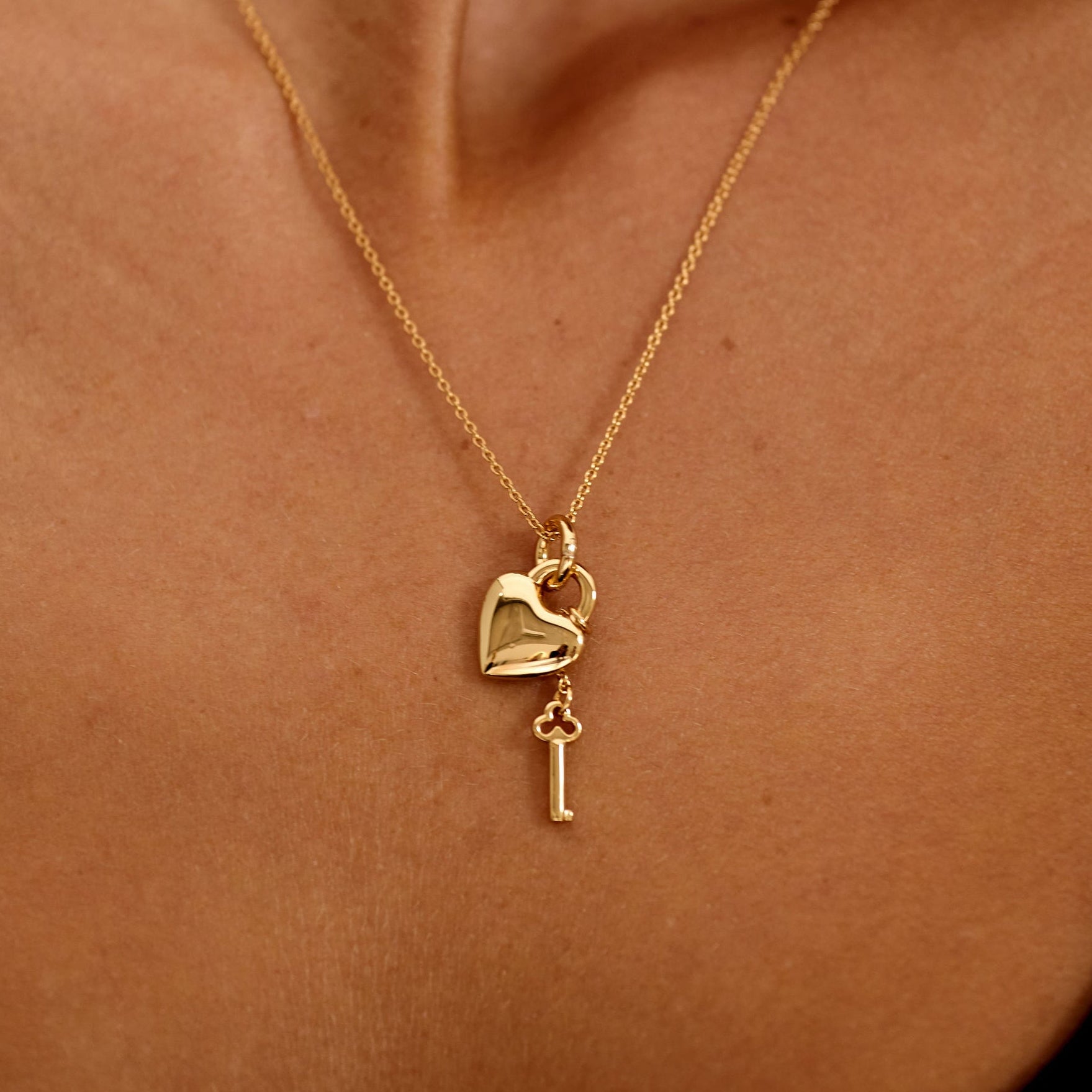 Gold necklace with heart and key pendant on a person's neck