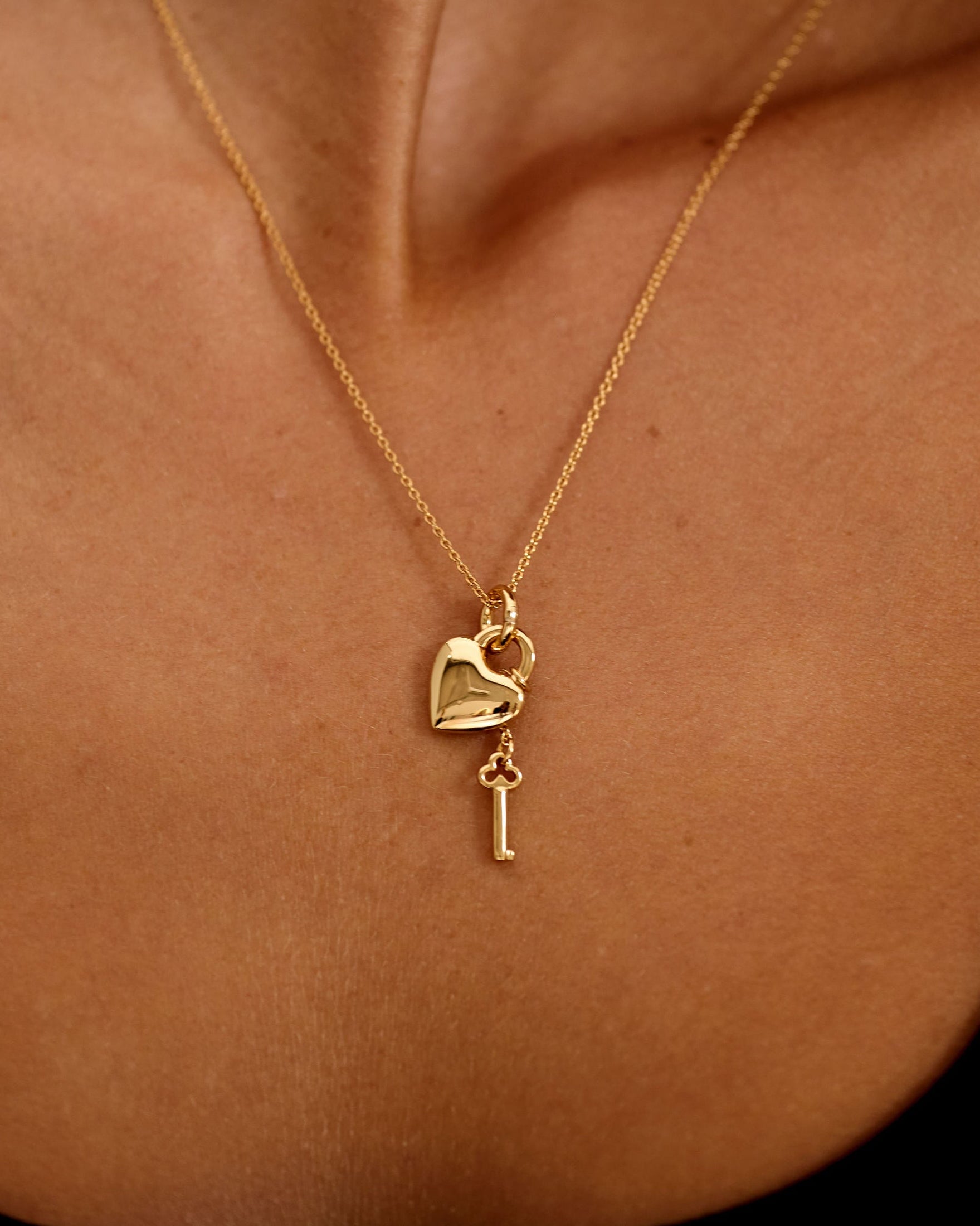 Gold necklace with heart and key pendant on a person's neck