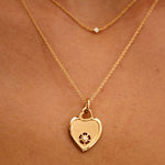 Gold heart-shaped necklace with a pendant on a person's neck against a brown background