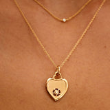 Gold heart-shaped necklace with a pendant on a person's neck against a brown background