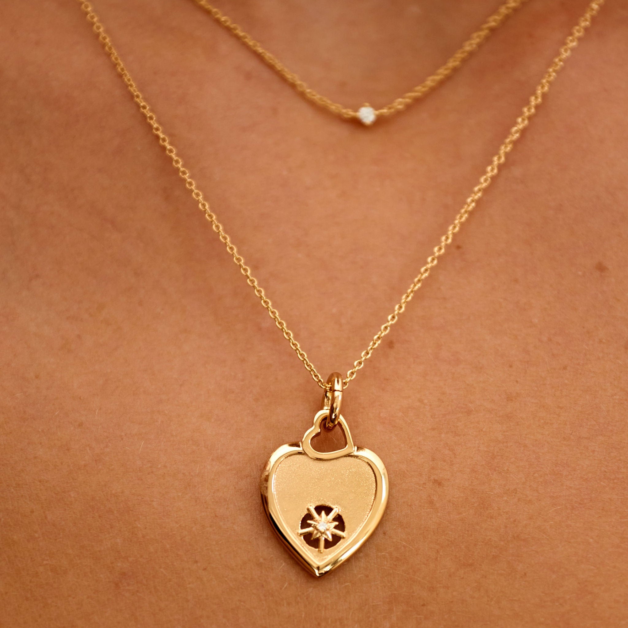 Gold heart-shaped necklace with a pendant on a person's neck against a brown background