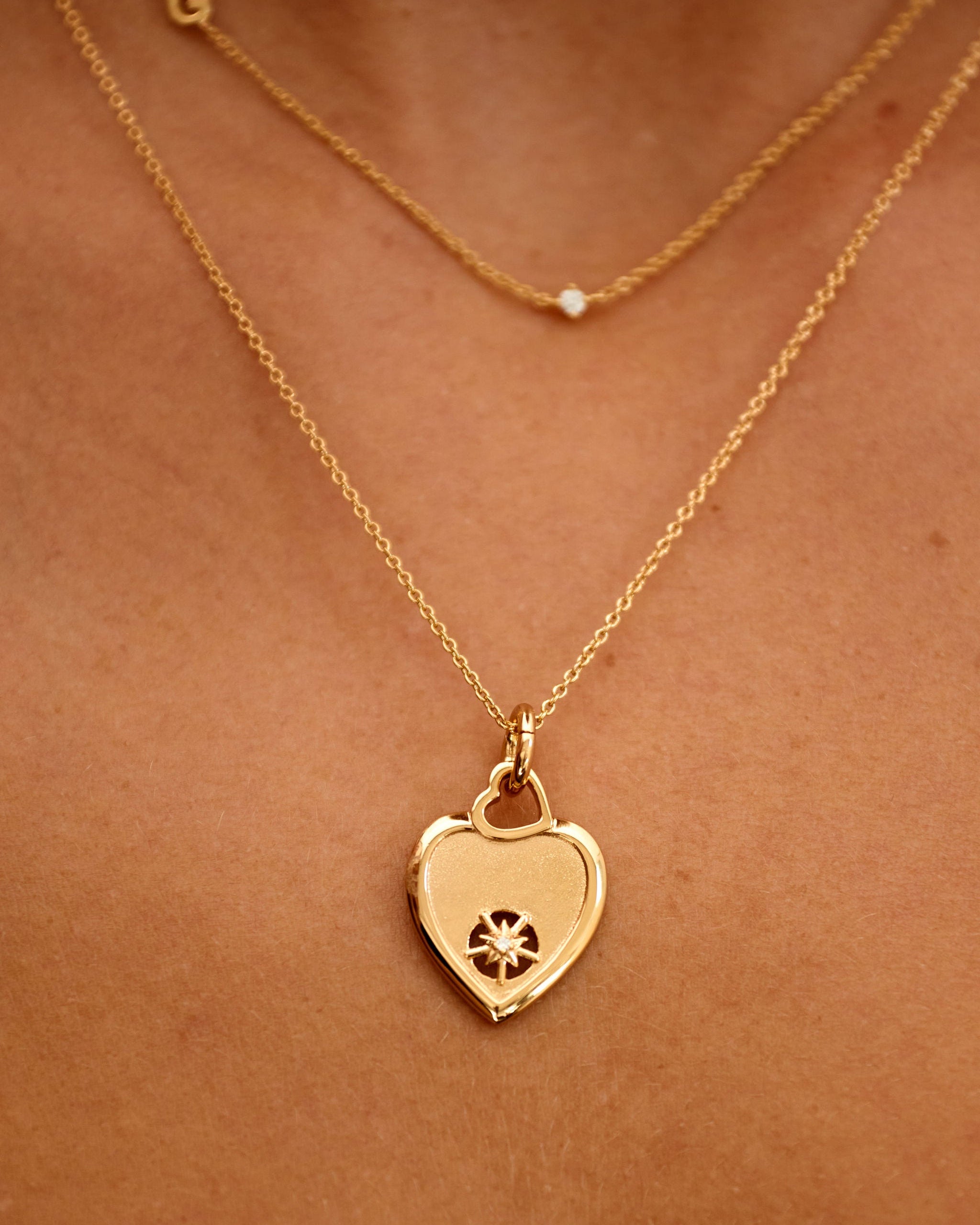 Gold heart-shaped necklace with a pendant on a person's neck against a brown background