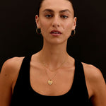 Woman wearing gold necklaces and hoop earrings against a black background