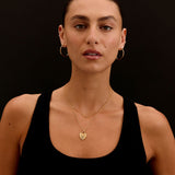 Woman wearing gold necklaces and hoop earrings against a black background