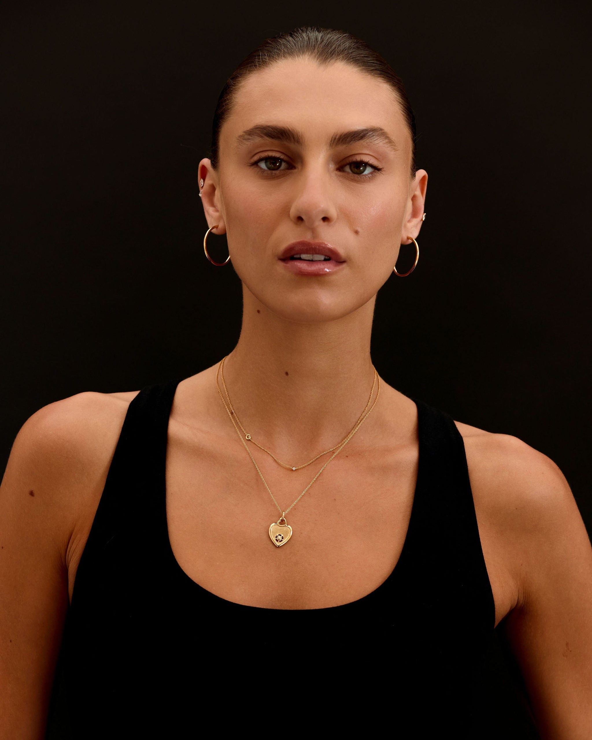 Woman wearing gold necklaces and hoop earrings against a black background