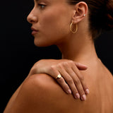 Woman with gold hoop earrings and ring on a black background