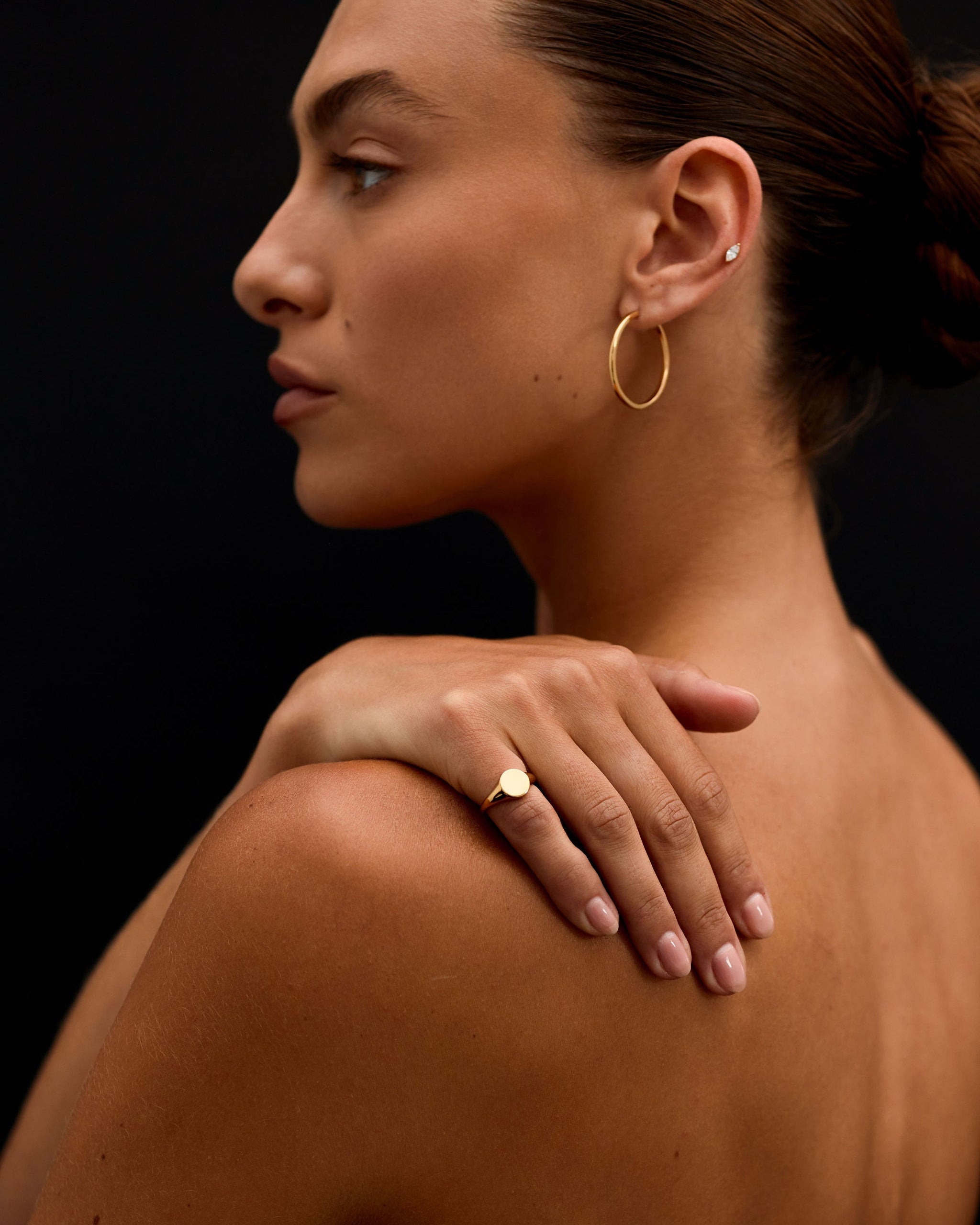 Woman with gold hoop earrings and ring on a black background