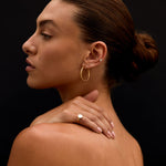 Woman with a bun, wearing gold earrings and a ring, against a black background