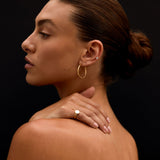 Woman with a bun, wearing gold earrings and a ring, against a black background