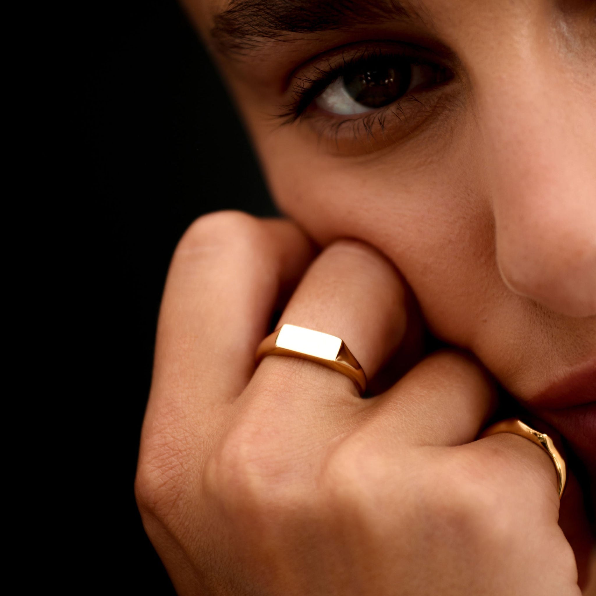 Close-up of a person with a gold ring on their finger against a dark background