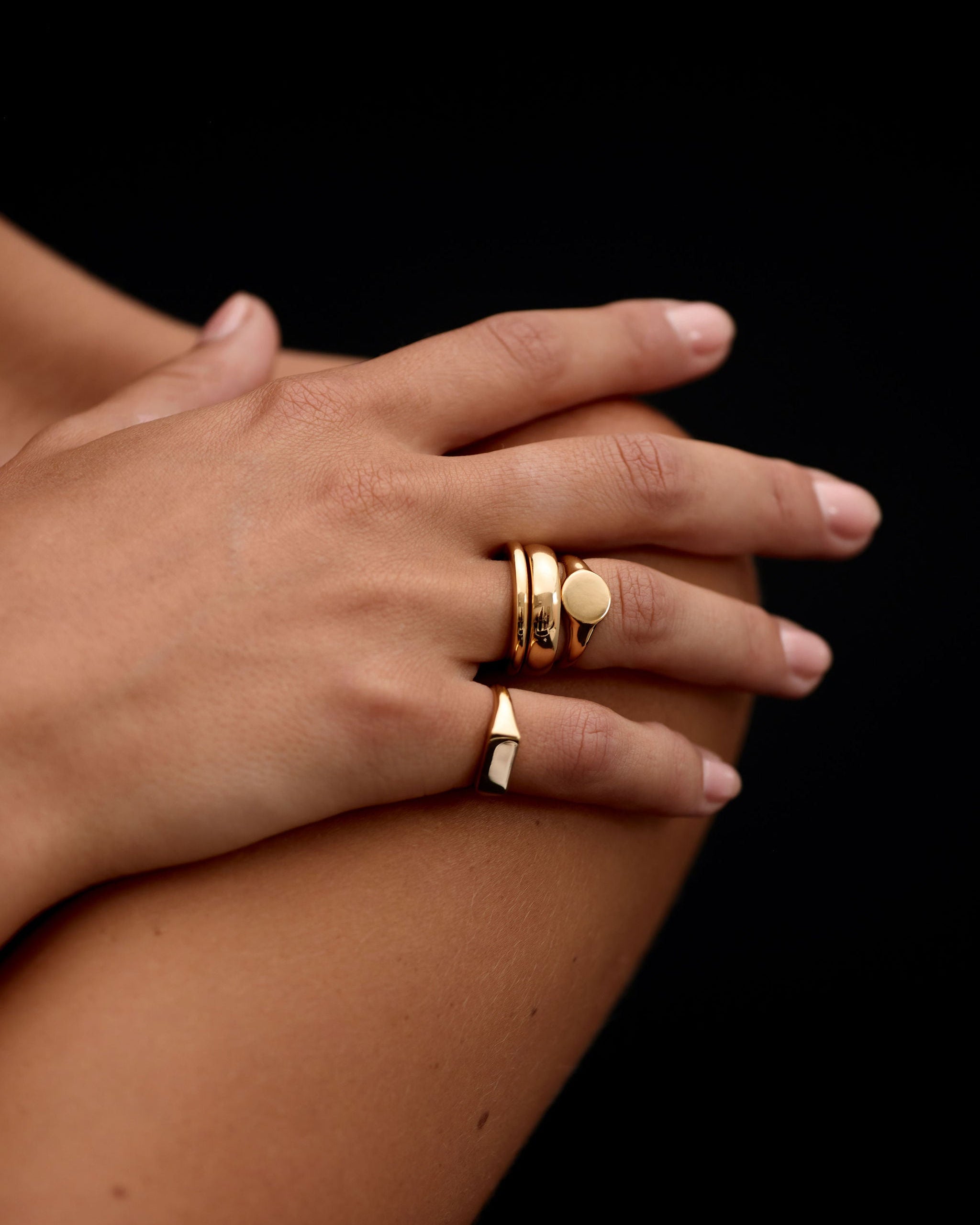 Hand wearing gold rings on a black background
