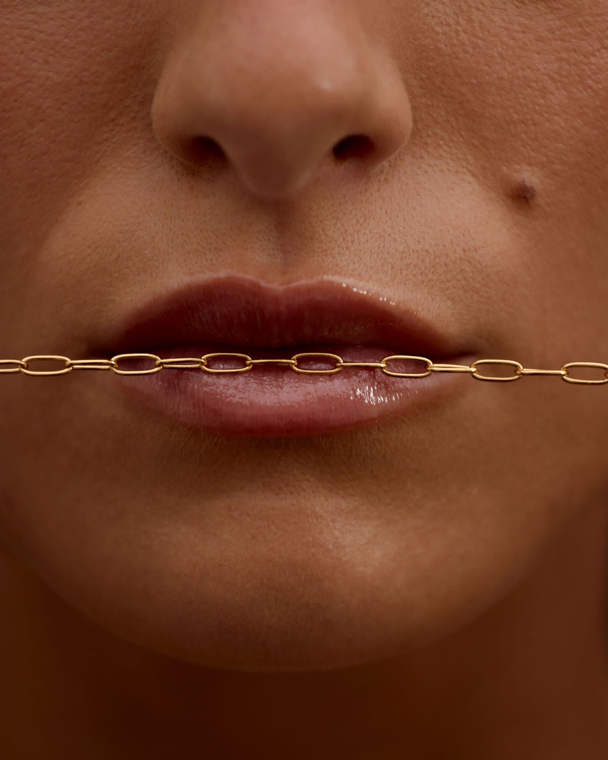 Close-up of a person's mouth with a gold chain over it