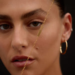 Close-up of a person wearing gold hoop earrings and a necklace against a dark background
