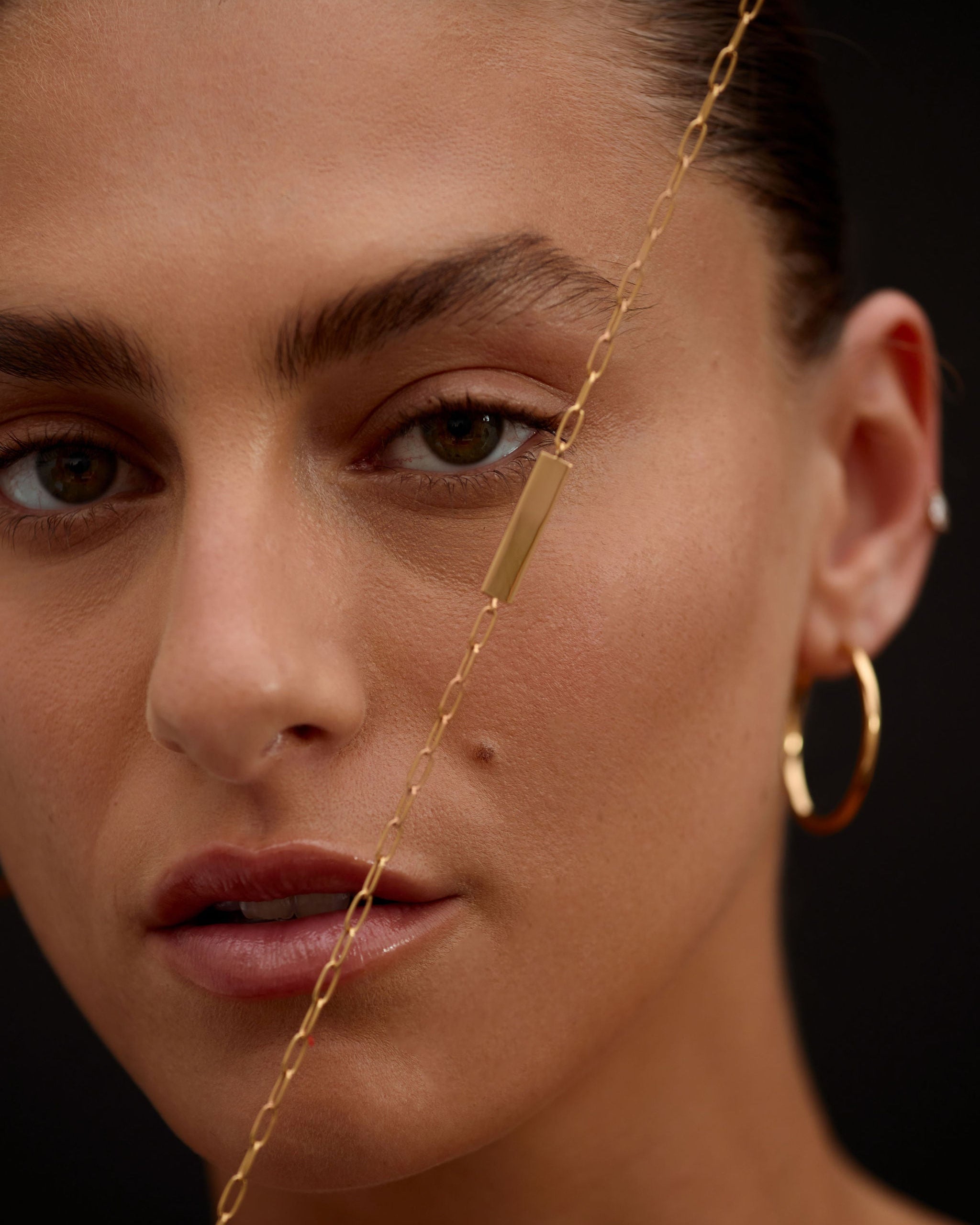 Close-up of a person wearing gold hoop earrings and a necklace against a dark background