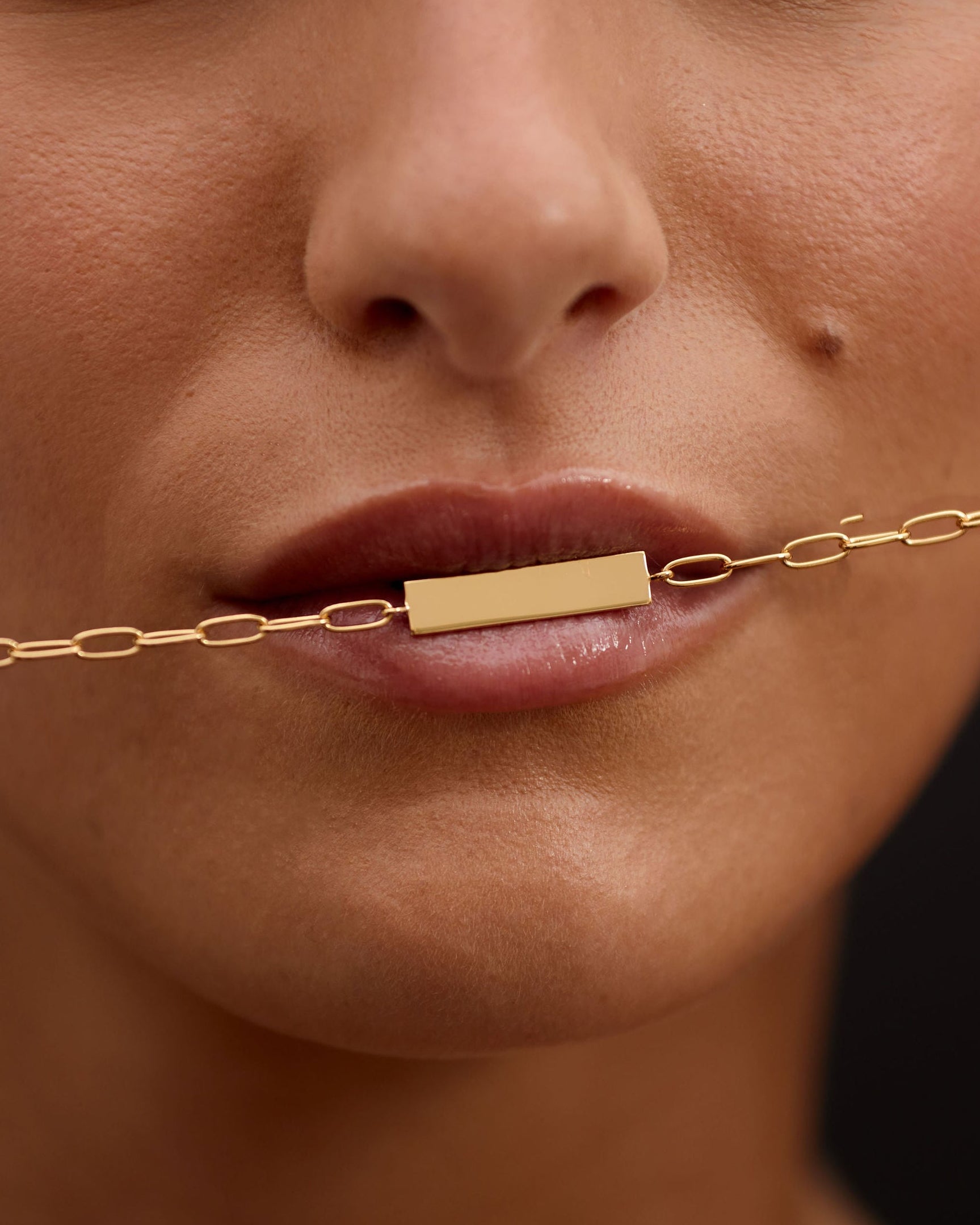 Close-up of a woman's face with a gold bar necklace.