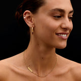 Woman wearing a gold necklace and earring against a black background