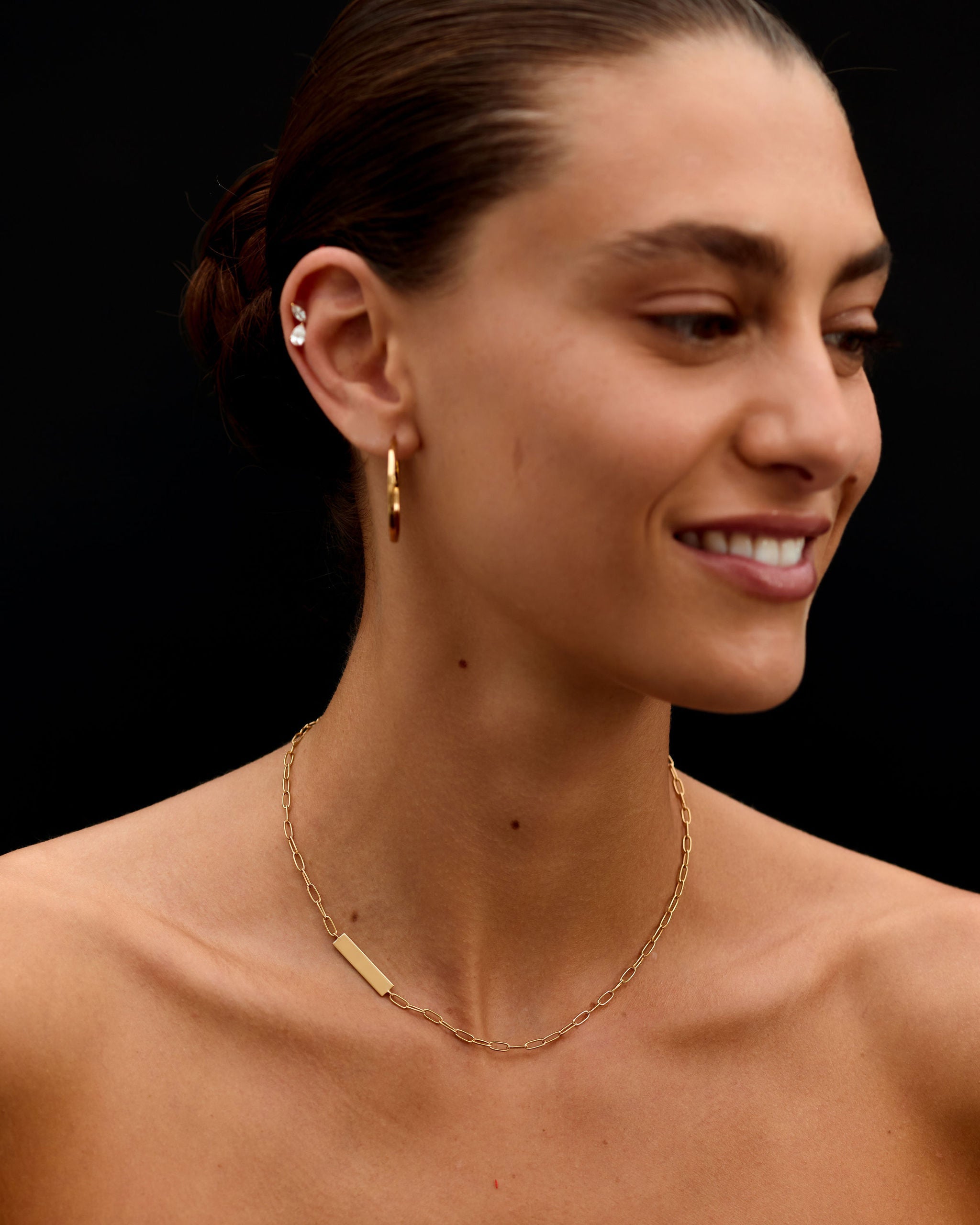 Woman wearing a gold necklace and earring against a black background