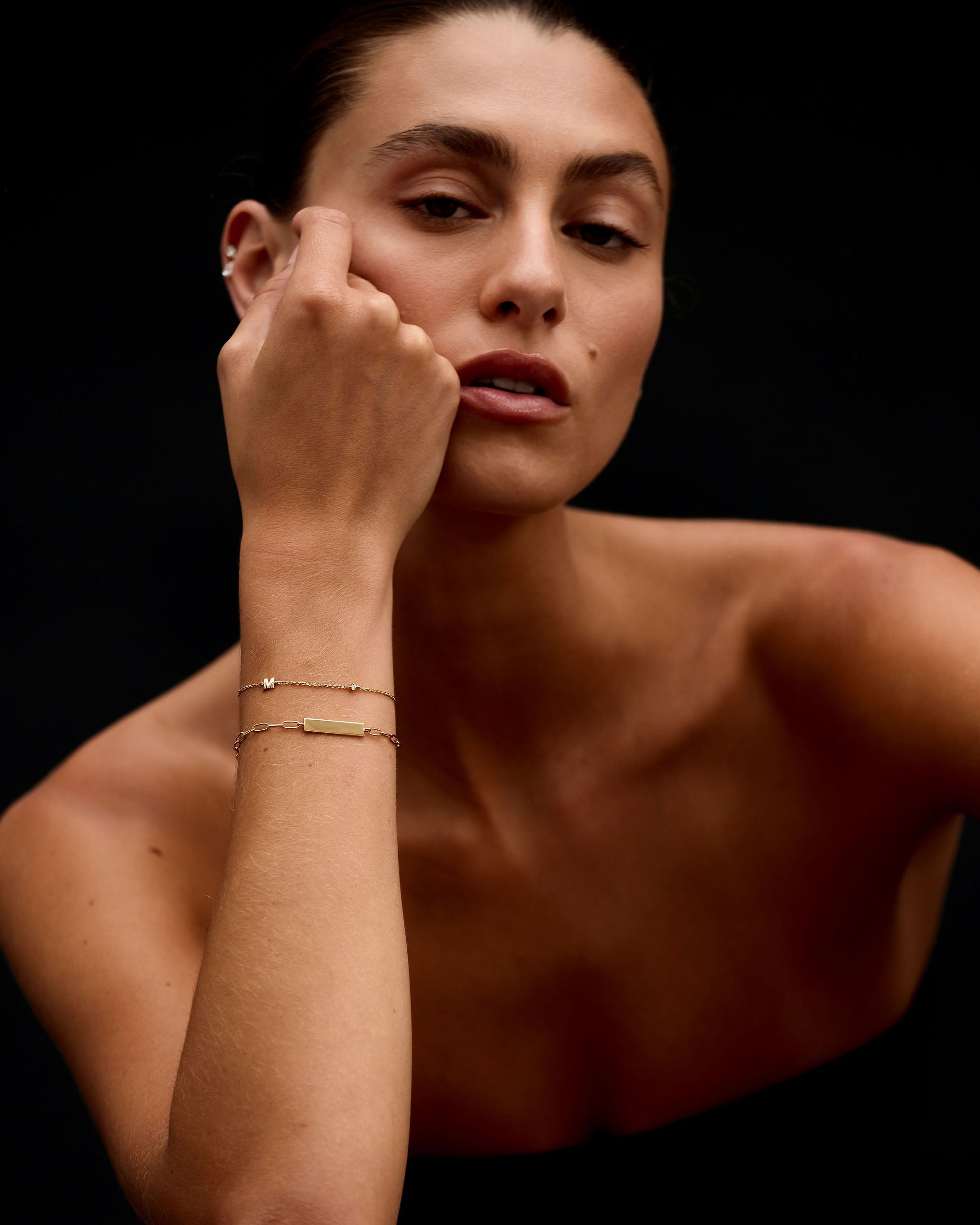 Woman with a gold bracelet on her wrist against a black background