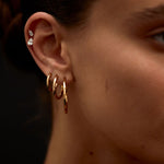 Close-up of a person's ear with gold hoop earrings and a blurred background