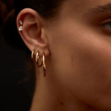 Close-up of a person's ear with gold hoop earrings and a blurred background