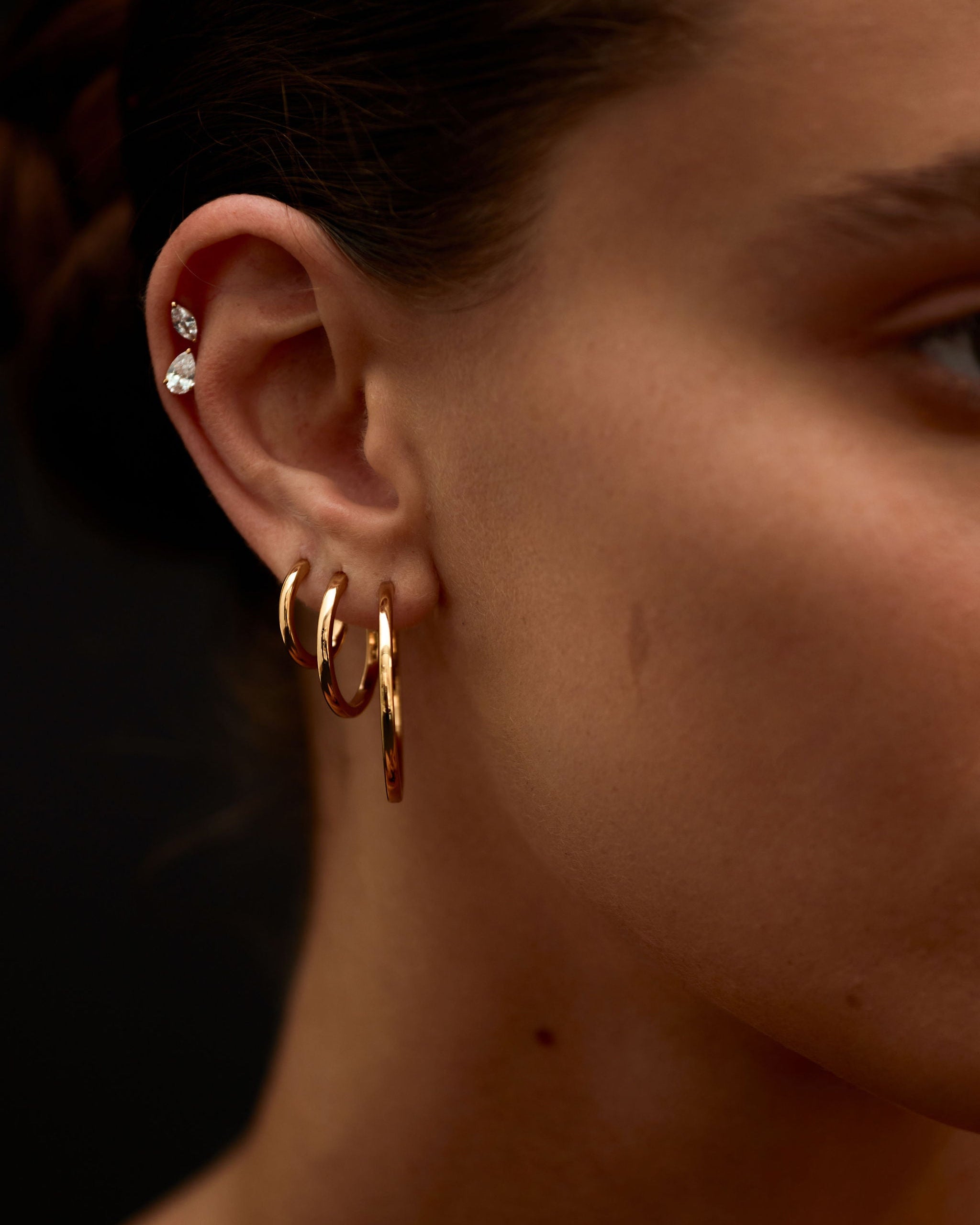 Close-up of a person's ear with gold hoop earrings and a blurred background