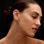 Close-up of a woman's neck and ear with gold earrings against a black background