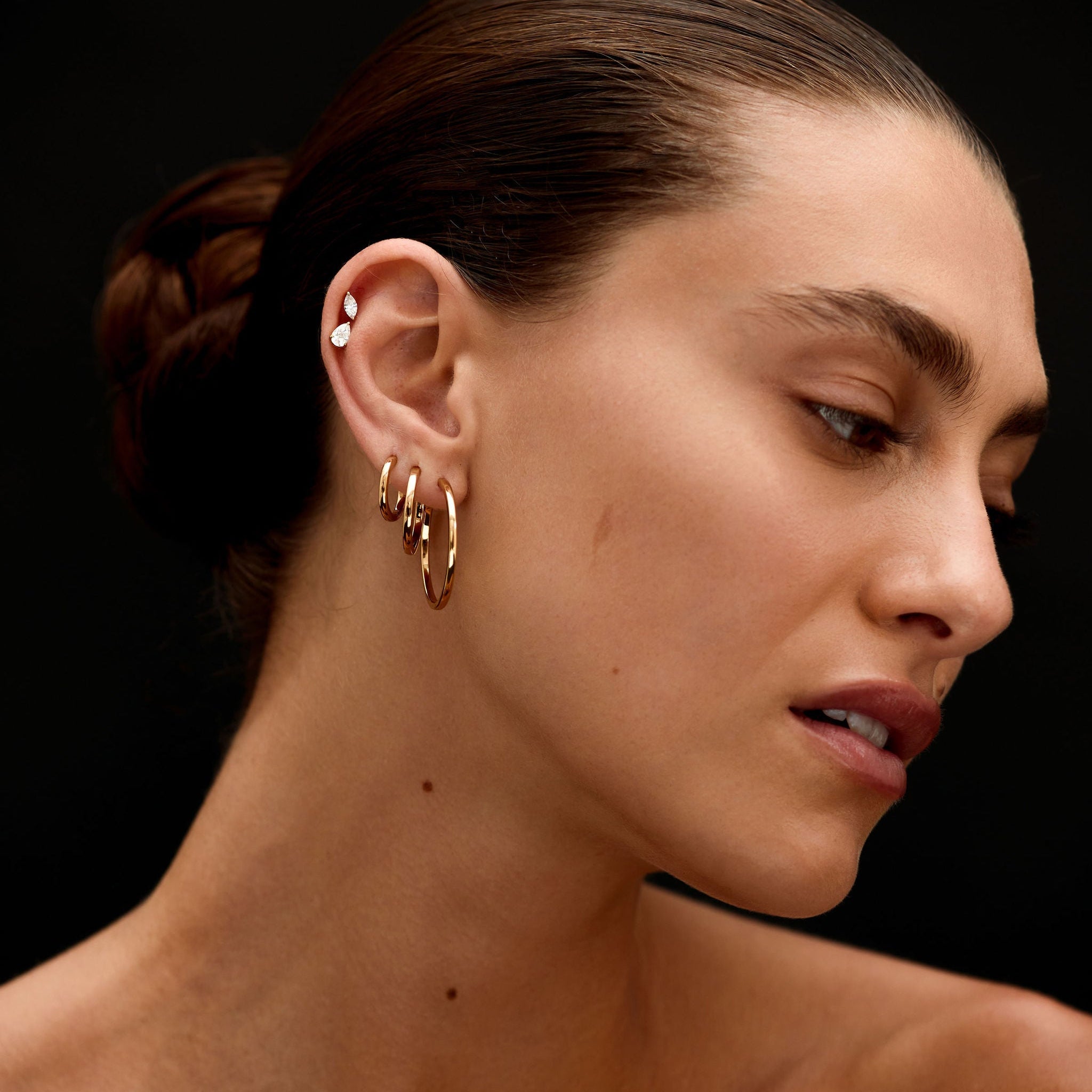 Close-up of a woman's neck and ear with gold earrings against a black background