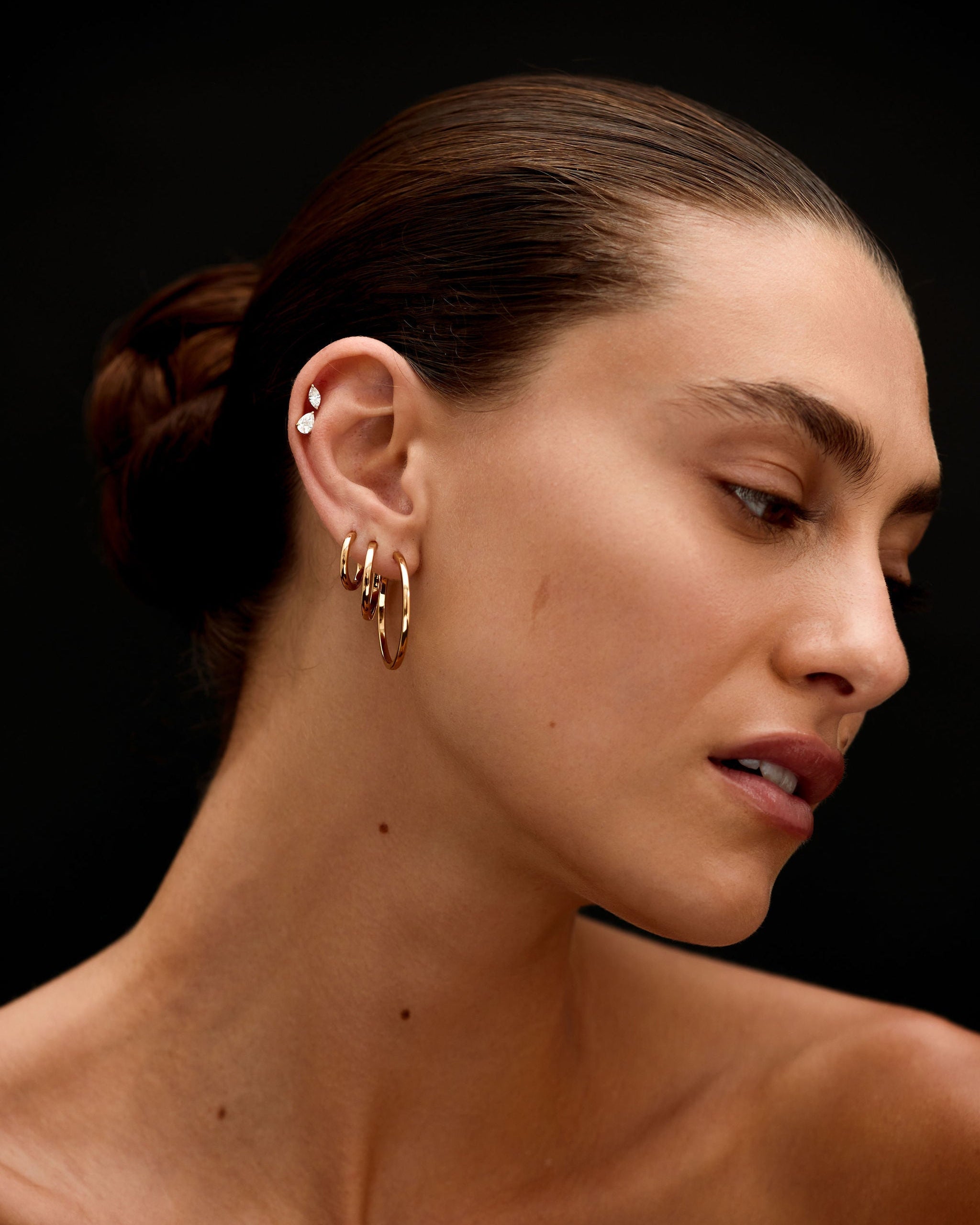 Close-up of a woman's neck and ear with gold earrings against a black background