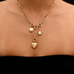 Gold necklace with heart and star charms on a person against a black background