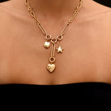 Gold necklace with heart and star charms on a person against a black background