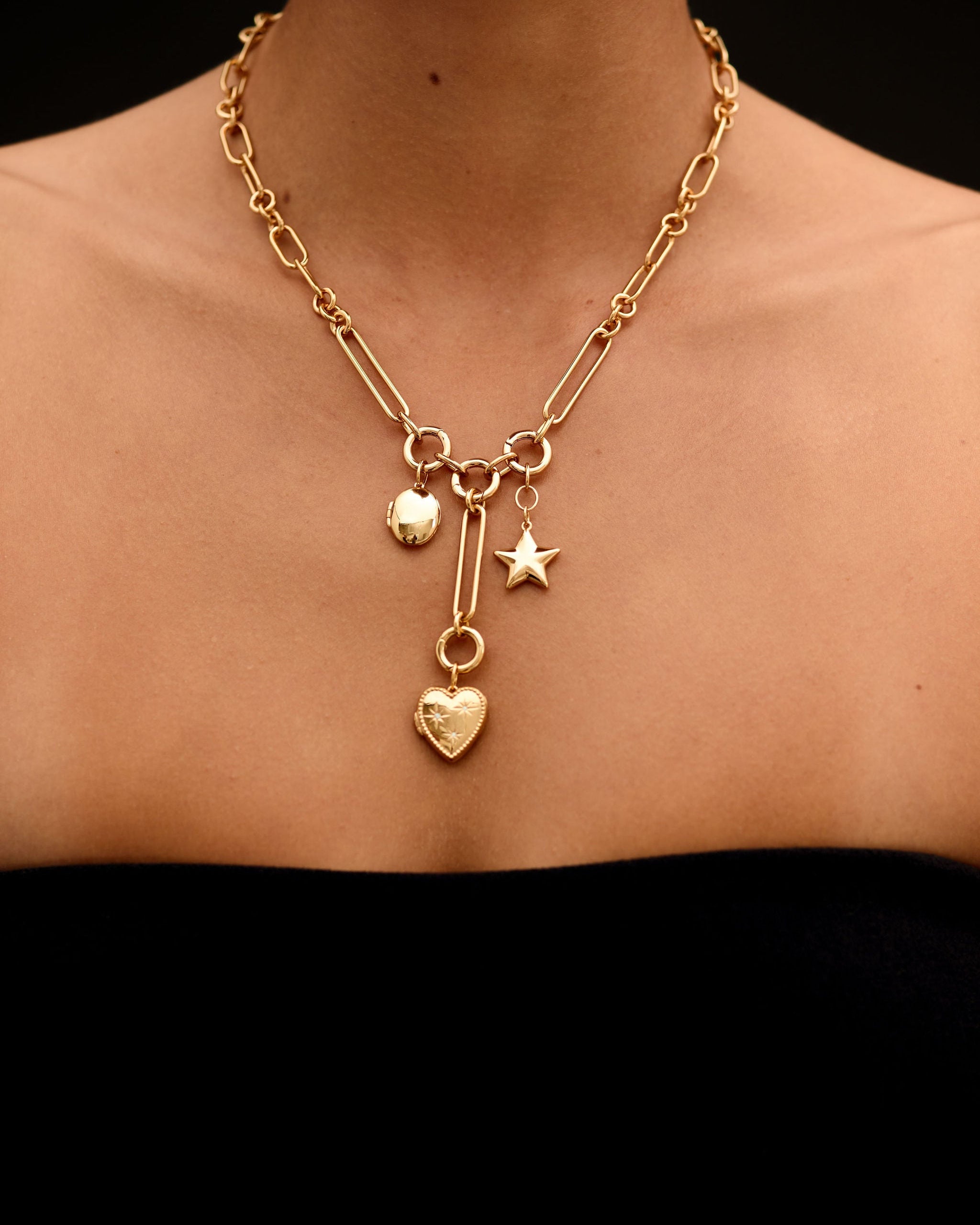 Gold necklace with heart and star charms on a person against a black background