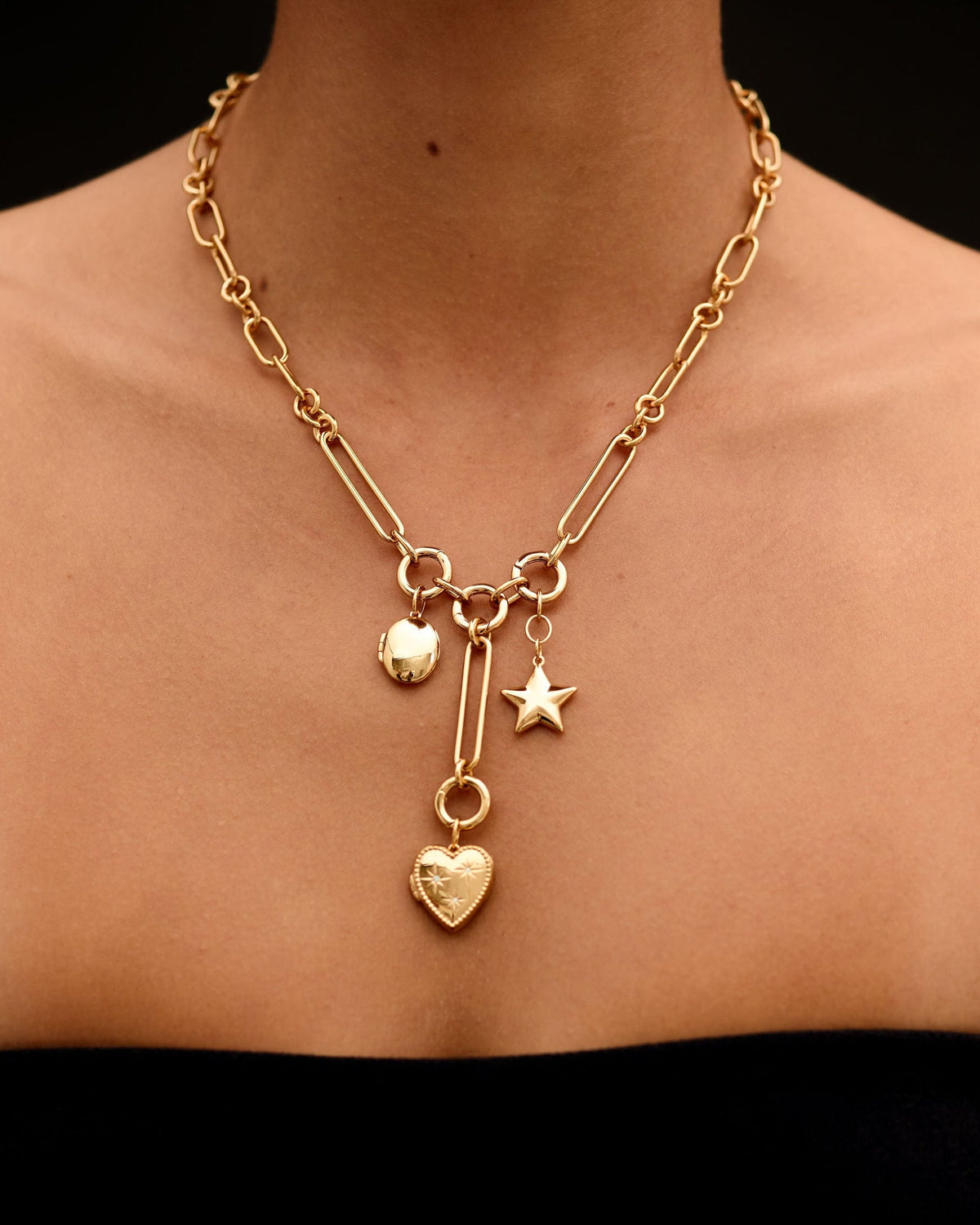 Gold necklace with heart and star charms on a person against a black background