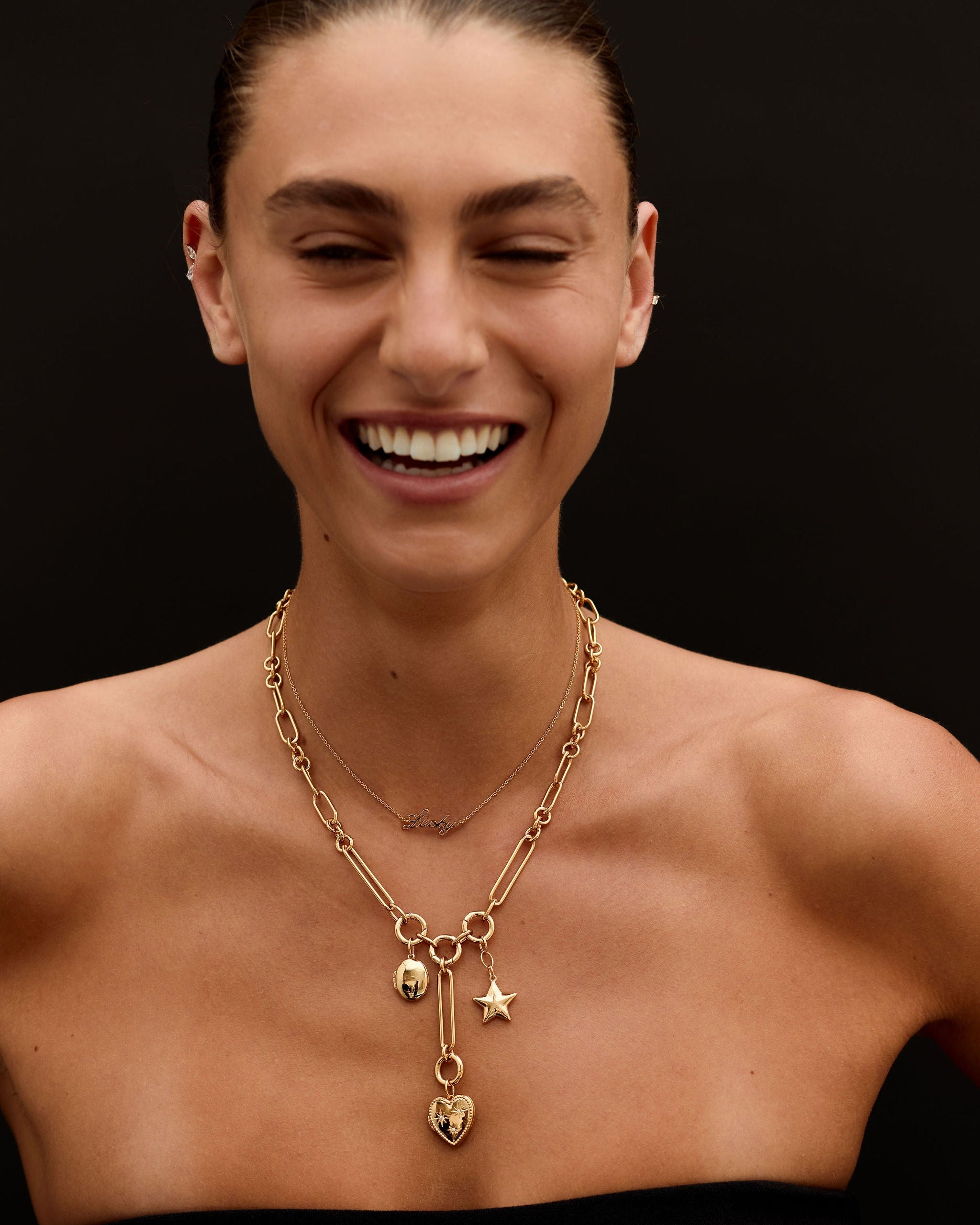 Woman wearing a gold necklace with heart and star charms on a black background