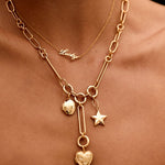 Gold necklace with heart and star charms on a person's neck against a black background