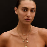 Woman wearing a gold necklace with heart and star pendants against a black background