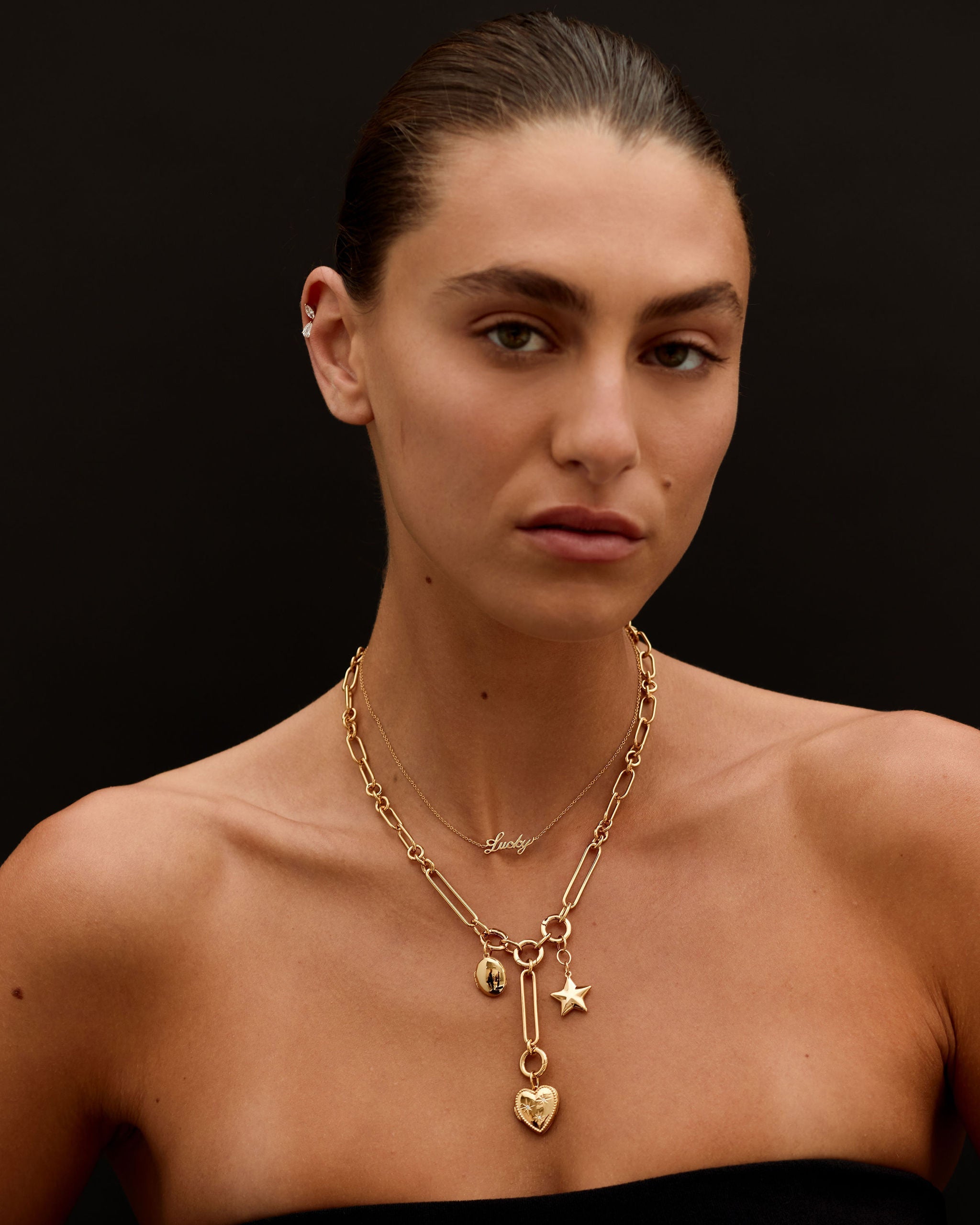 Woman wearing a gold necklace with heart and star pendants against a black background
