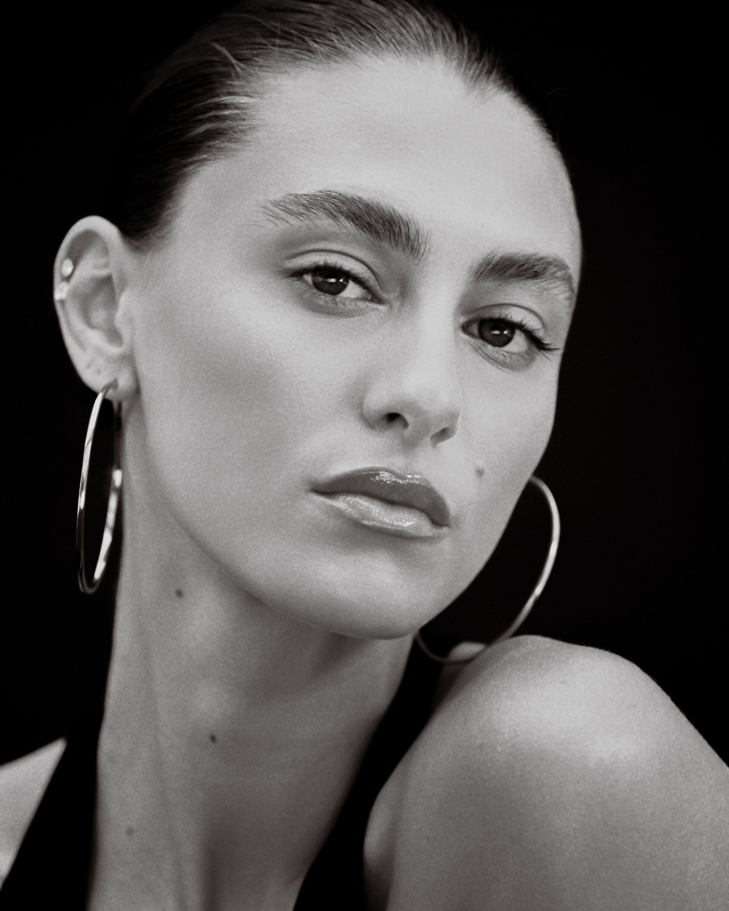 Black and white portrait of a woman wearing hoop earrings against a black background