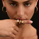 Woman wearing gold hoop earrings and rings on a black background