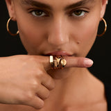 Woman wearing gold hoop earrings and rings on a black background