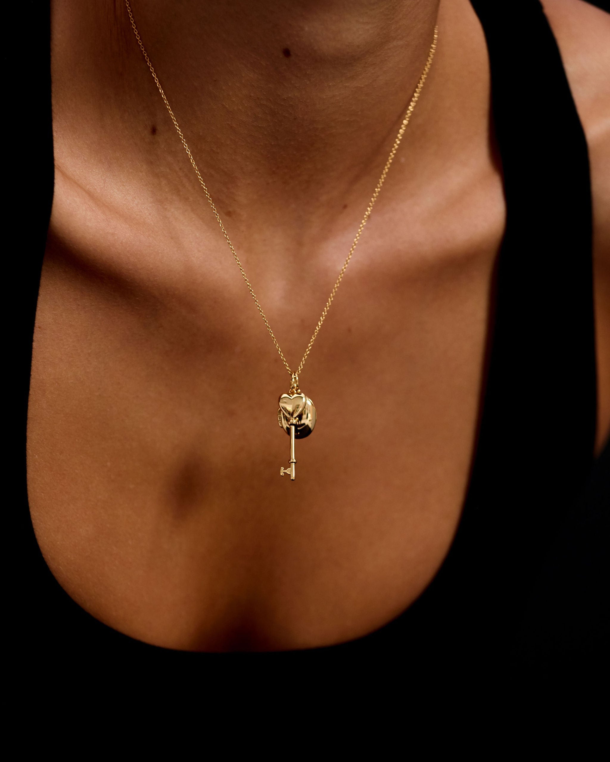 Gold necklace with a heart and key pendant on a person's neck against a black background